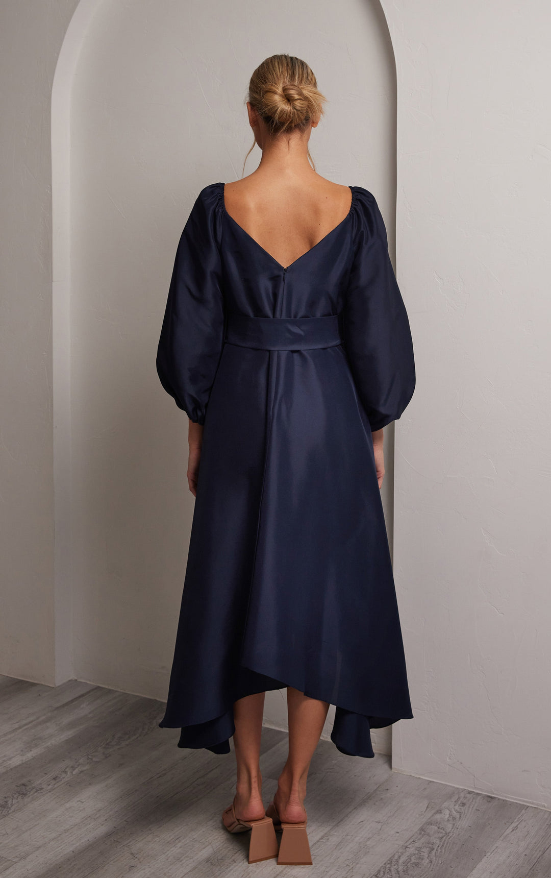 back view of woman wearing silk navy dress with puffed sleeves and tie at front