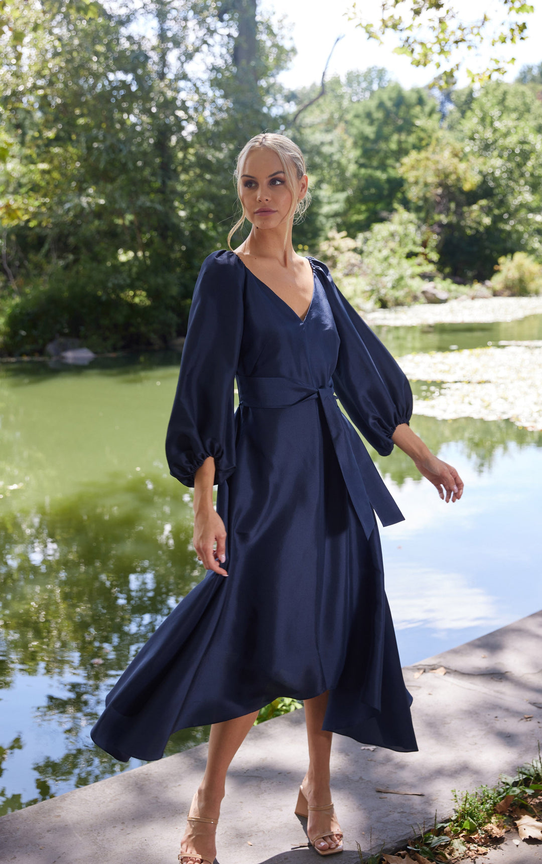 woman outside wearing silk navy dress with puffed sleeves and tie at front