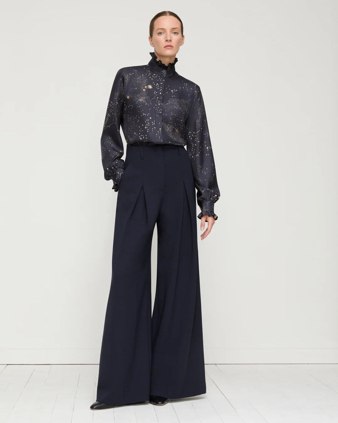 Person wearing a dark patterned blouse and black wide-leg pants on a white background